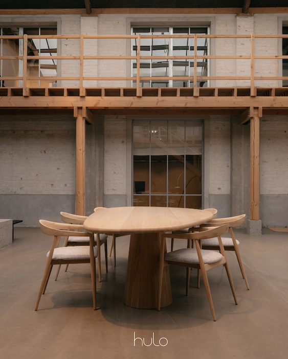 Tafel massief eik met organische tafelblad. Onderstel kegelvormig. Rond de tafel staan houten stoelen. foto genomen in industrieel kader