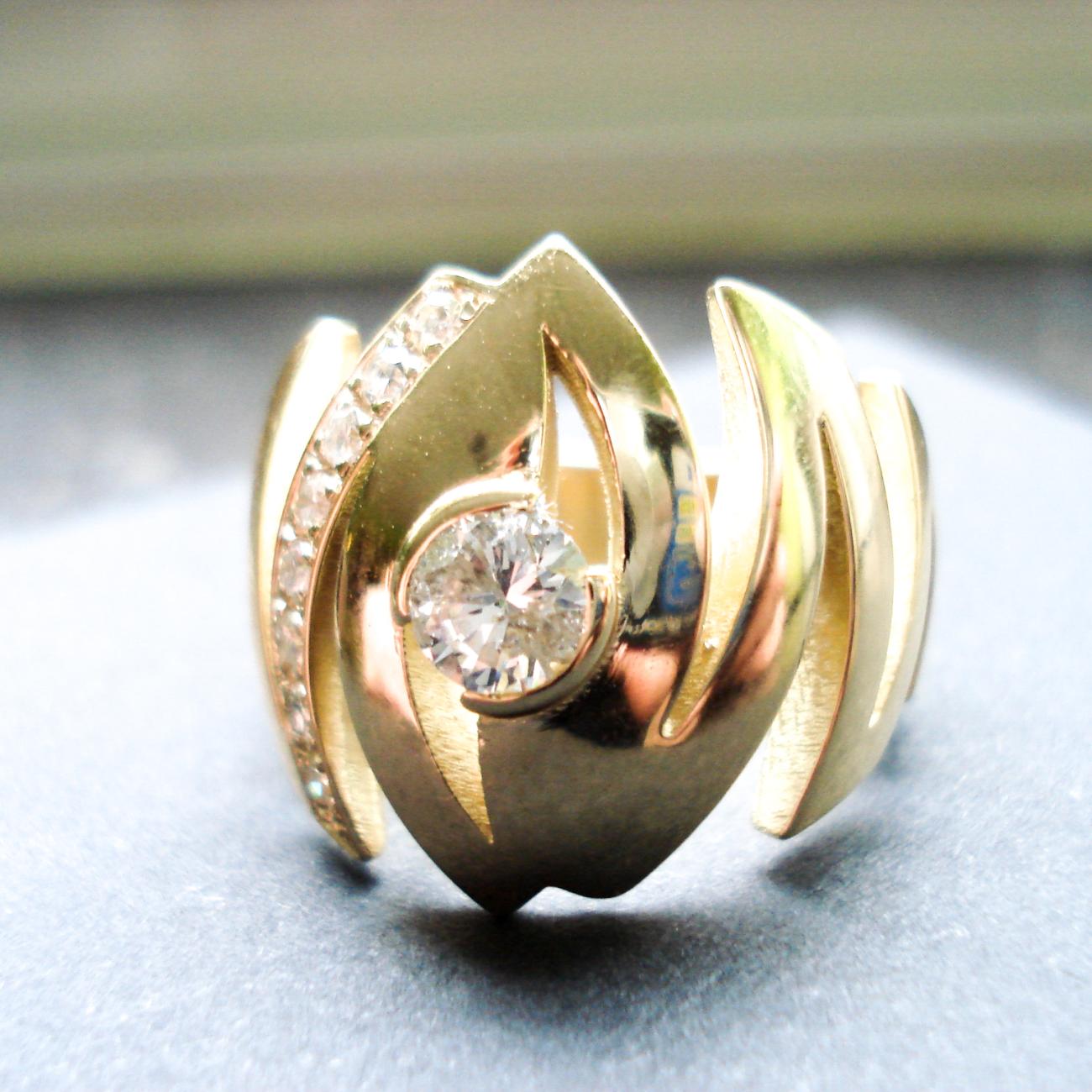 Soliede ring, vervaardigd uit het oud Goud en diamanten van de klant. De ring evolueert, in een zigzagbeweging, van boven naar onderen naar smaller toe. Zo creëren we een brede, grote ring die toch heel comfortabel draagt. De grote steen is centraal gezet in een halfopen kastzetting. Aan 1 kant vindt je een mooie kasteelzetting van 10x2pt.