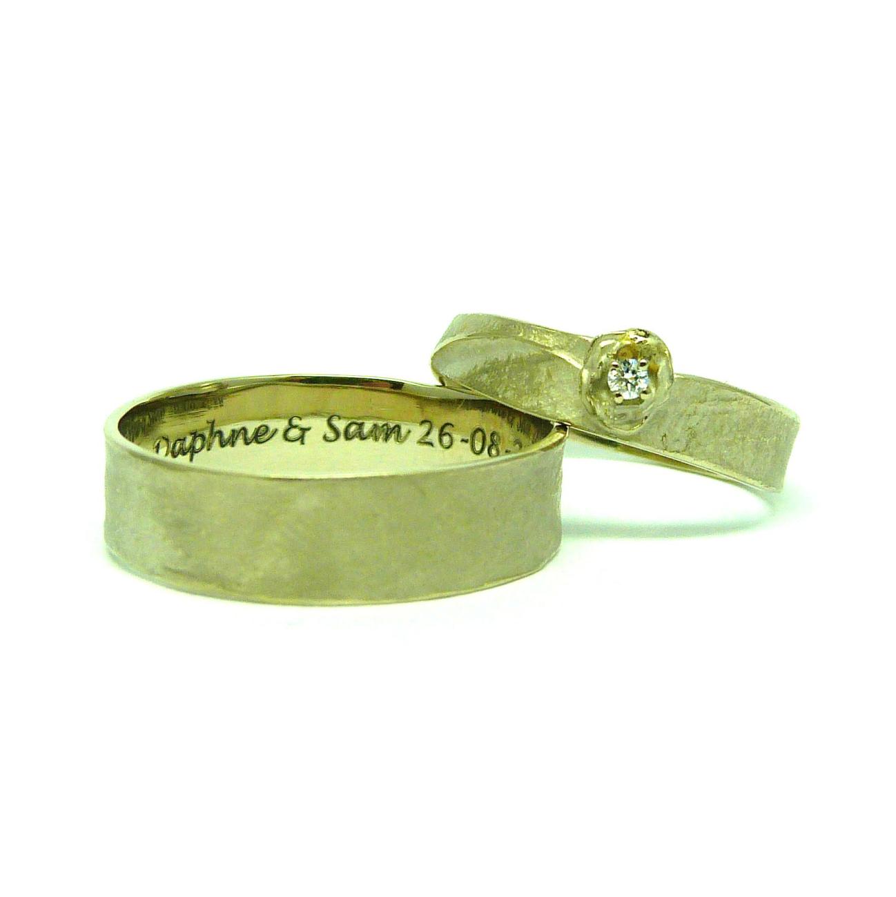Bij het smeden ontstaat de overlapping in haar ring. Iets over de rand een roosje met een diamant Voor hem een eenvoudige ring, ietsje breder. Champagne Wit Goud - Diamant