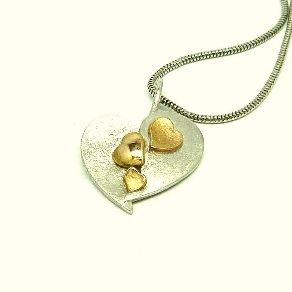 Deze hanger symboliseert de verbinding van mama, papa en 3 kinderen. Het grote witgouden hart bestaat uit twee helften, ze symboliseren man en vrouw De helften liggen ietwat verschoven naast elkaar, maar liggen deels ook over/onder elkaar, dit staat voor het leven/relatie met zijn mooie maar ook moeilijke momenten. De verbinding van man en vrouw wordt bekroond met drie kinderen, hier vertolkt door de 3 Rosé Gouden hartjes die mooi in het midden zowel op moeders als op vaderskant liggen.