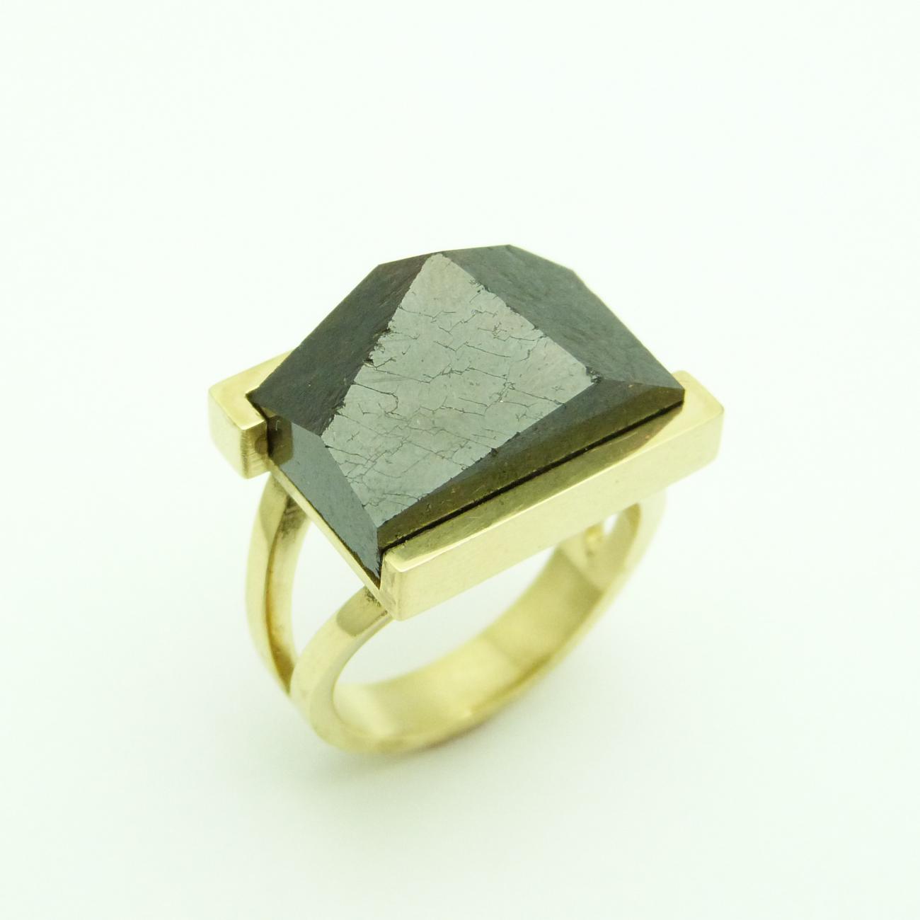 In een nieuwe fase in haar leven wordt de nieuwe liefde bezegeld met deze ring. Zij kocht ooit, op een groezelig marktje in Laos, een ruwe granaat. Wij lieten de steen slijpen tot een mooie grote rechthoekige steen volgens de afmetingen van de Gulden Snede, symbool voor de oneindigheid der dingen. Enkele vlakken zijn gepolijst, anderen niet, als symbool voor het leven en de liefde met zijn zachte maar ook ruwere kanten. Haar nieuwe liefde betaalde de ring met het inruilen van zijn oud goud en zo is de