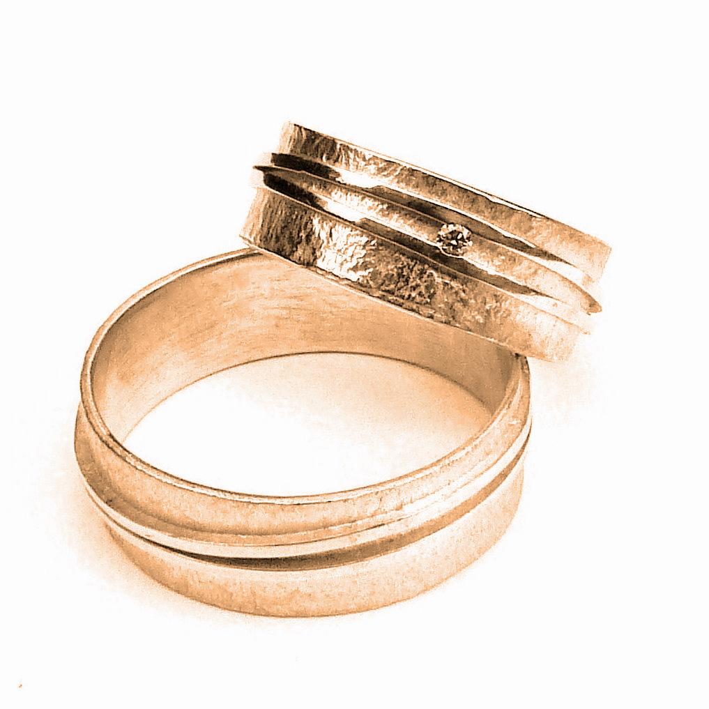 Twee strakke bandjes die een vloeiende beweging maken rondom de met de hamer bewerkte ringen Met voor haar heel subtiel een diamantje. Palladium Wit Goud - Diamant