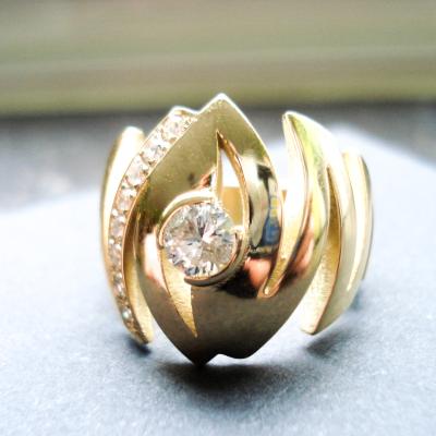 Soliede ring, vervaardigd uit het oud Goud en diamanten van de klant. De ring evolueert, in een zigzagbeweging, van boven naar onderen naar smaller toe.  Zo creëren we een brede, grote ring die toch heel comfortabel draagt.  De grote steen is centraal gezet in een halfopen kastzetting. Aan 1 kant vindt je een mooie kasteelzetting van 10x2pt.